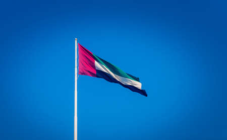 The flag of the United Arab Emirates waving on the mast against the blue sky.の写真素材