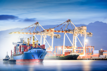 Logistics and transportation of international container cargo ship with ports crane bridge in harbor at dusk for logistics import export background and transportation industryの写真素材