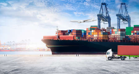 Container cargo freight ship during discharging at industrial port move to container yard by trucks, handlers, cargo plane, copy space, logistic import export background and transport industry conceptの写真素材