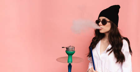 A young woman in a hipster image smokes a hookah, sheesha and enjoys smoking. Place for your text.の写真素材