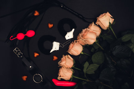 Various sex toys set on a black background. Top view. Spring. Roses.