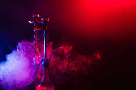 Modern hookah, shisha on a smoky black background with colored lighting and smoke. Close-up and place for your textの写真素材