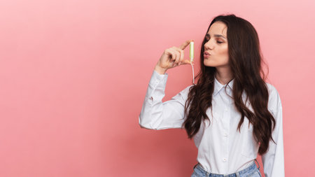 A young woman holds a menstrual swab with an applicator in her hands for easy use. Pink background....