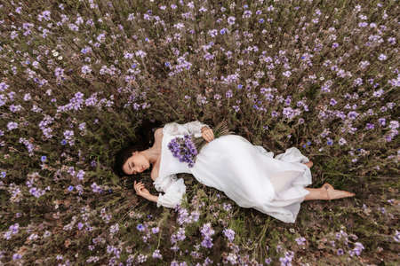 A young beautiful girl lies with her eyes closed in a blooming field of Provence. Romantic atmosphereの写真素材