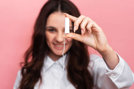 A young woman holds a menstrual swab with an applicator in her hands for easy use. Pink background. close-up. The concept of feminine hygiene.の写真素材