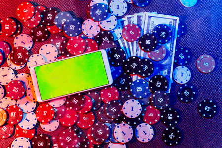 The concept of an online casino: betting chips and a smartphone with a green background with a copy space. Top view. Smoke added to the photoの写真素材