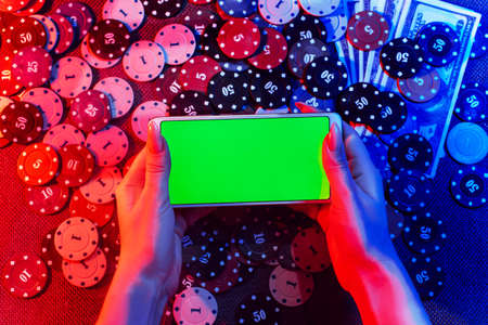 The concept of an online casino: playing cards, betting chips and a smartphone with a copy space in womens hands. Top view. Smoke added to the photoの写真素材