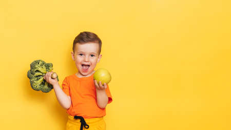 A studio shot of a boy holding a fresh broccoli and a green apple. The concept of healthy baby food....