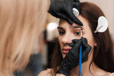 The beautician-brovist gives shape by applying henna with a brush, coloring the eyebrows in a beauty...