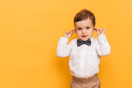 A studio shot of a cute little boy grimacing stands on a yellow background. Funny kidの写真素材