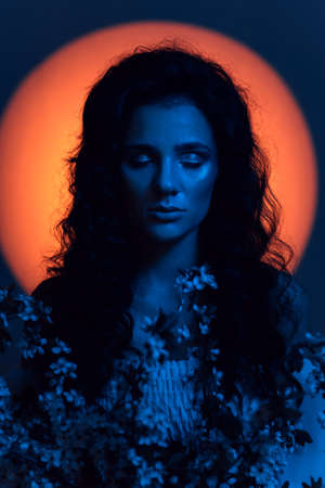 Portrait of a girl who looks like a nymph, in neon lighting with a halo over her head and flowers in...