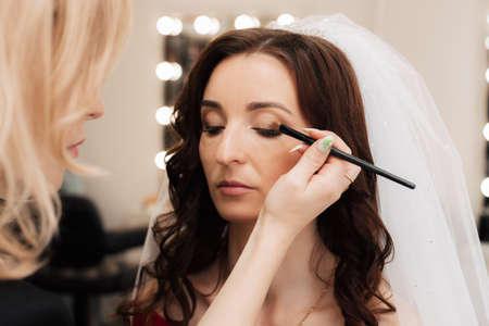 Girl makeup artist brush to apply eye shadow on the eyelid of the woman model. Close-upの写真素材