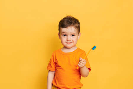 Happy baby toddler boy brushing his teeth with a toothbrush on a yellow background. Health care, oral hygiene.の写真素材