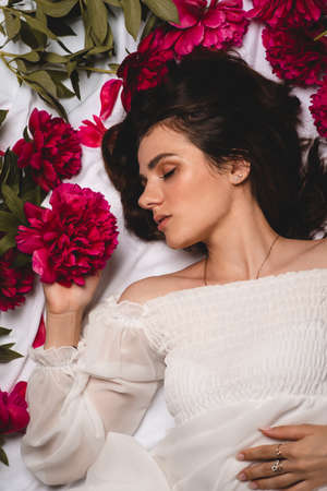 portrait of a young, peaceful and gentle girl lying surrounded by scattered flowers, peonies. Top viewの写真素材