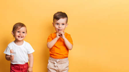 Little brother and sister are eating a sweet lollipop on a stick. Yellow background. The concept of...