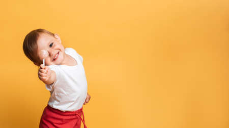 little girl is eating a sweet lollipop on a stick. Yellow background. The concept of prevention of...