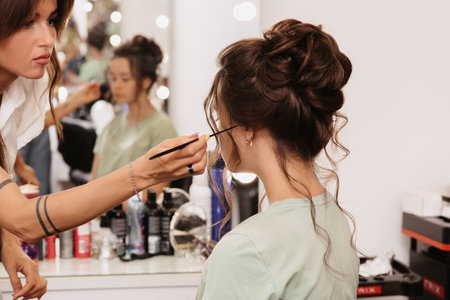 Shooting in a beauty salon. A hair stylist corrects the hairstyle of a young dark-haired girl with a...