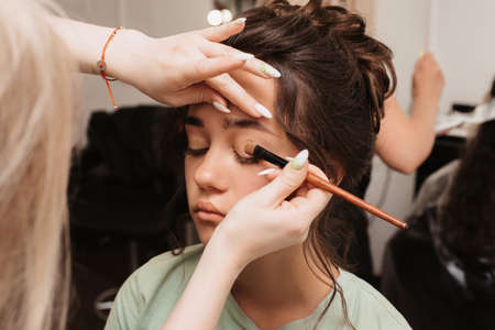 Shooting in a beauty salon. The makeup artist applies a shiny pigment to the eyes with a fluffy brush.の写真素材