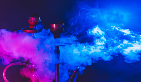 Modern hookah, shisha on a smoky black background with colored lighting and smoke. Close-up and place for your textの写真素材