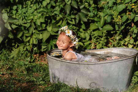 A cute smiling baby is bathing in a bathtub standing in the garden, on a hot sunny summer dayの写真素材