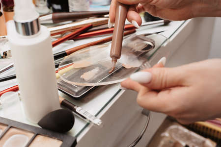 Shooting in a beauty salon. A picture of the hands of a makeup artist against the background of the workplace, with professional cosmetics and brushes laid out.の写真素材