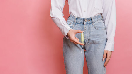 A young woman holds a menstrual swab in her hands. Pink background. Space for text. The concept of feminine hygiene.の写真素材