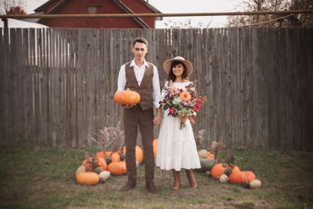 A young couple gently holds hands on each other. A man stands with a pumpkin in his hands, and a girl with a bouquet. Autumn environmentの写真素材