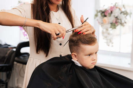 Shooting in a beauty salon. A barber cuts a little boys hair with scissorsの写真素材