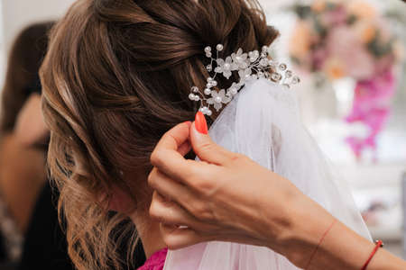 The hairdresser makes an elegant hairstyle for the brides styling with white jewelry in her hair in the salonの写真素材