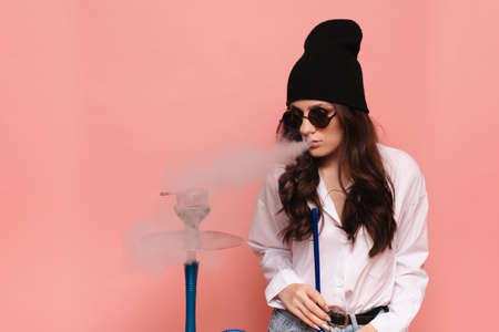 A young woman in a hipster image smokes a hookah, sheesha and enjoys smoking.の写真素材