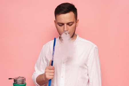 A male model smokes a hookah, sheesha and enjoys it. Pink backgroundの写真素材