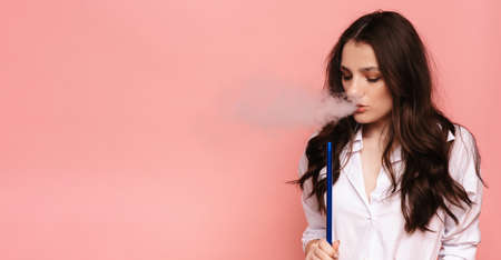 Young, beautiful girl smokes a hookah, shisha. It produces smoke from his mouth. The pleasure of smoking. Place for your text.の写真素材
