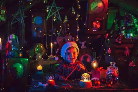 A fabulous, Christmas atmosphere. A little boy, Santas assistant, at the tables with gifts. New Year decorations. Postcard.の写真素材
