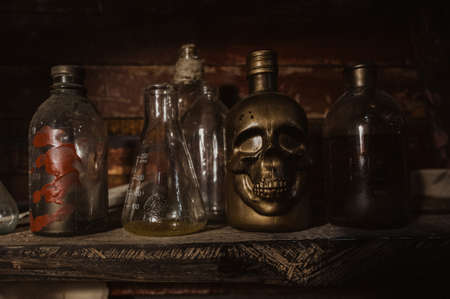 Old glass bottles, jars and flasks stand on a dark shelf in the hold of the ship next to the skull.の写真素材
