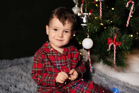 A child boy in a Christmas pajamas near a Christmas tree decorated with Christmas decorationsの写真素材