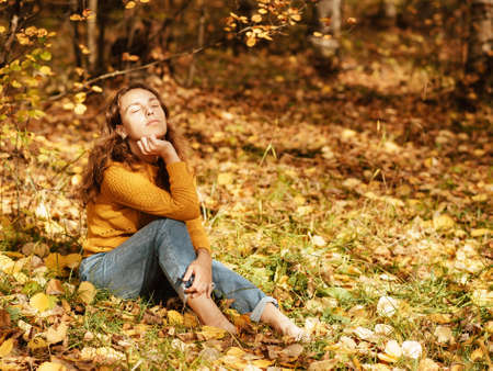 beautiful girl in autumn Park sitting on fallen leavesの写真素材