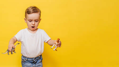 Cute laughing little boy on a yellow background with a dinosaur toy in his hands. Copy space.の写真素材
