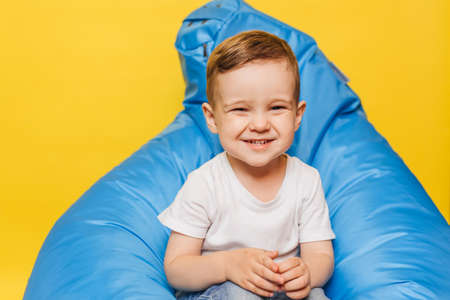 Laughing little boy on a yellow background sitting in a blue chair.の写真素材