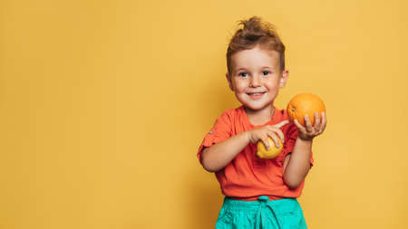 Studio shot of a smiling boy holding a fresh lemon and orange on a yellow background. The concept of healthy baby food, vitamin C. A place for your text.の写真素材