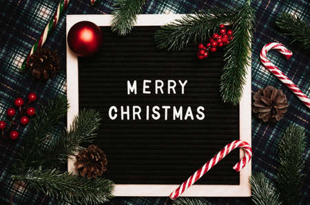 Merry Christmas lettering in plastic letters on an old vintage letter board. On the background there are caramel canes, balls, cones and fir branches. Top view. Flatley. Christmas greeting card.の写真素材