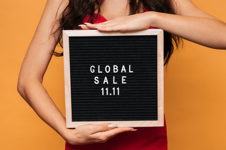 A letter board in womens hands with the inscription on it Global sale on November 11, isolated on a yellow background.の写真素材