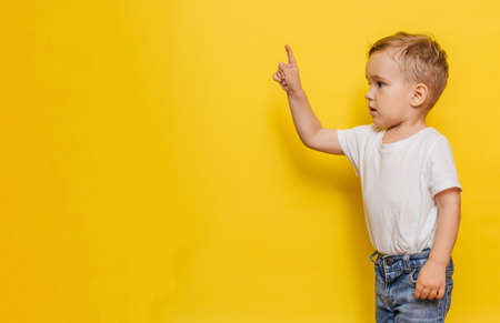 A little boy on a yellow background points to the background. Copy space.の写真素材