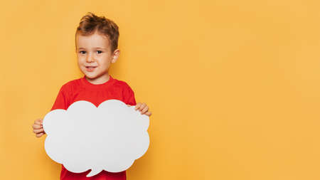 Studio portrait of a happy boy with a clean white board in the shape of a cloud on a bright yellow background, with a place for your text or advertisingの写真素材