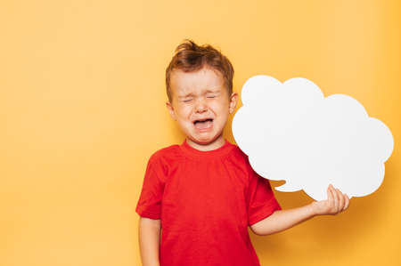 Studio portrait of a crying boy with a clean white board in the shape of a cloud on a bright yellow background, with a place for your text or advertisingの写真素材