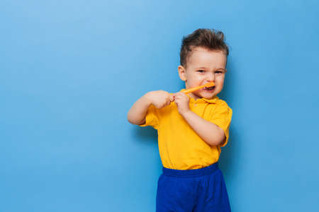 Happy child kid boy brushing teeth with toothbrush on blue background. Health care, dental hygiene. Mockupの写真素材
