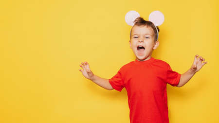 Studio portrait of a pampering Caucasian boy in a mouse costume on a bright yellow background, with a place for your text or advertisingの写真素材