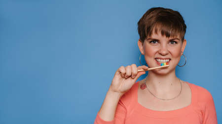A smiling young woman holds a natural bamboo toothbrush, isolated on a blue background. The concept of oral hygiene. A place for your text.の写真素材