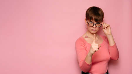 An angry, irritated young woman, isolated on a pink background, expresses dissatisfaction with her index finger. Human facial expressions, emotions. Body language. Copying space.の写真素材