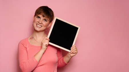Studio shot of a smiling young woman holding a blank letter board on a pink background. Copy space, space for your ad or text.の写真素材