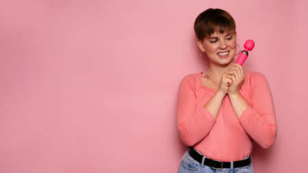 A studio shot of a young woman holding a pink female vibrator in her hands. Bright pink background. A place for your text or advertisement.の写真素材